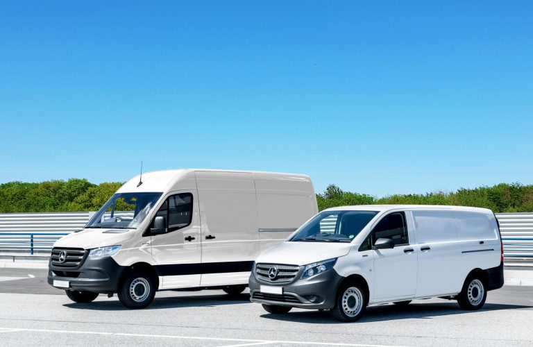 Two white delivery vans parked in a spacious parking lot under a clear blue sky.