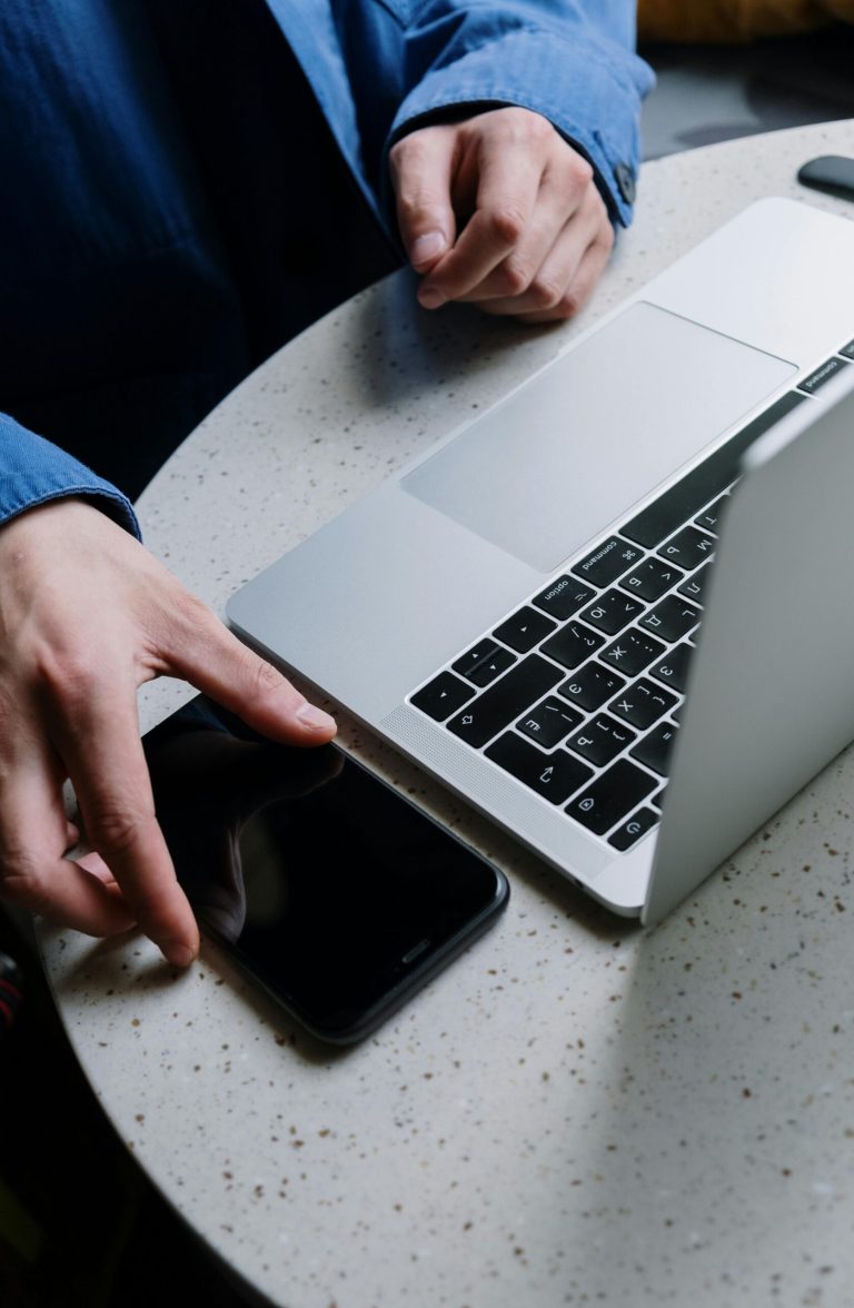 A close-up of hands exchanging phone next to a laptop on a round table.
